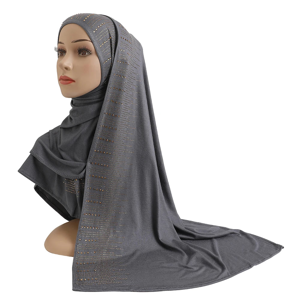 Une femme modèle un foulard en jersey de coton gris élégant avec des accents de diamants drapé sur sa tête et ses épaules.