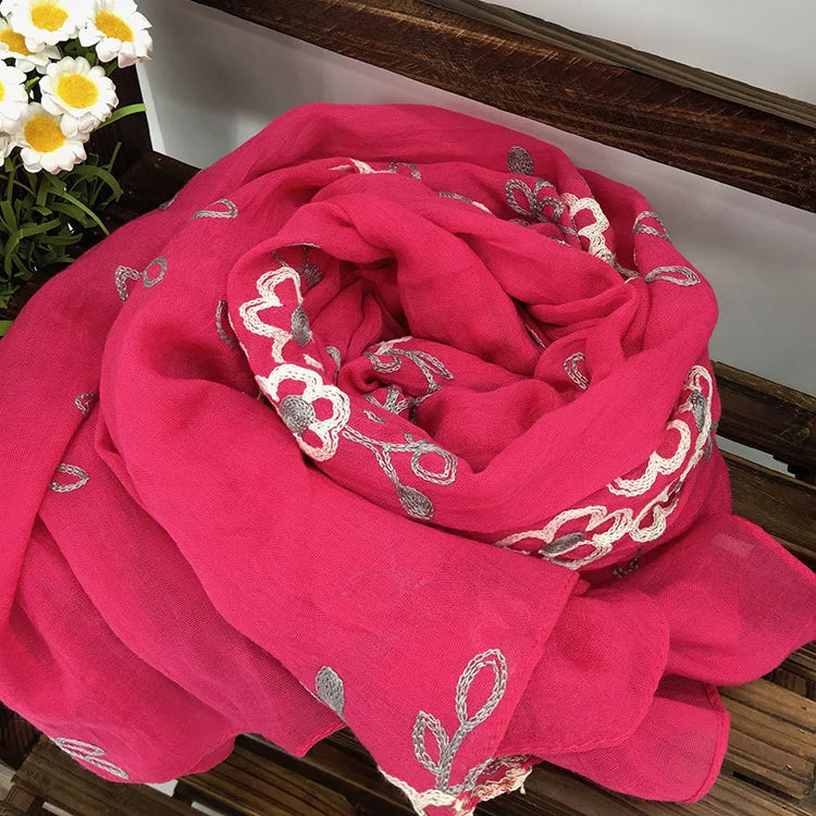Leuchtend rosa florales besticktes Wintertuch, aufgerollt auf einer Holzoberfläche.