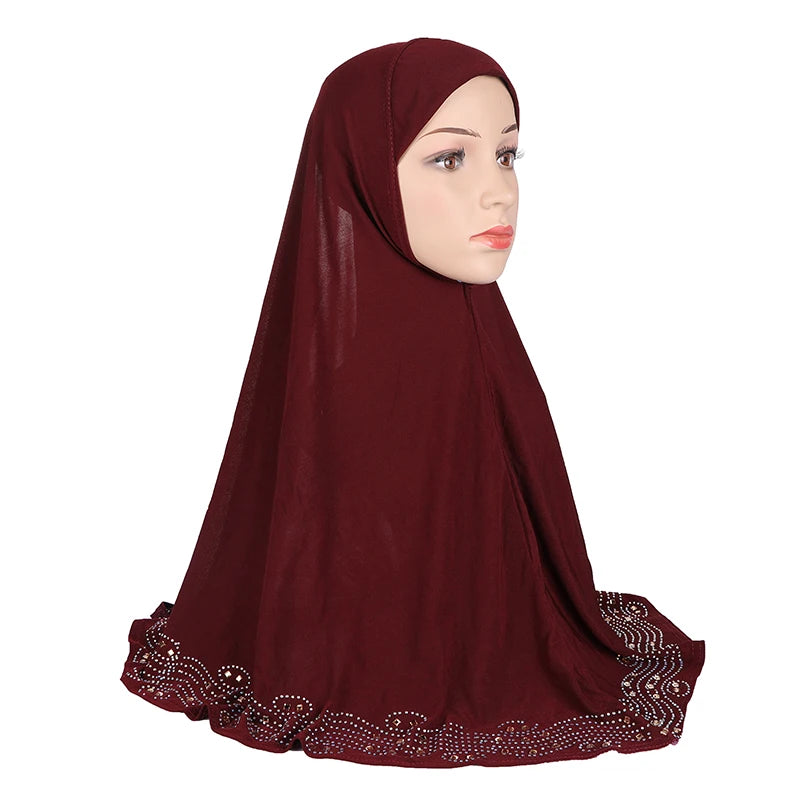 Eine Frau trägt einen dunkelroten, diamantbesetzten Hijab-Schal, in Profilansicht.
