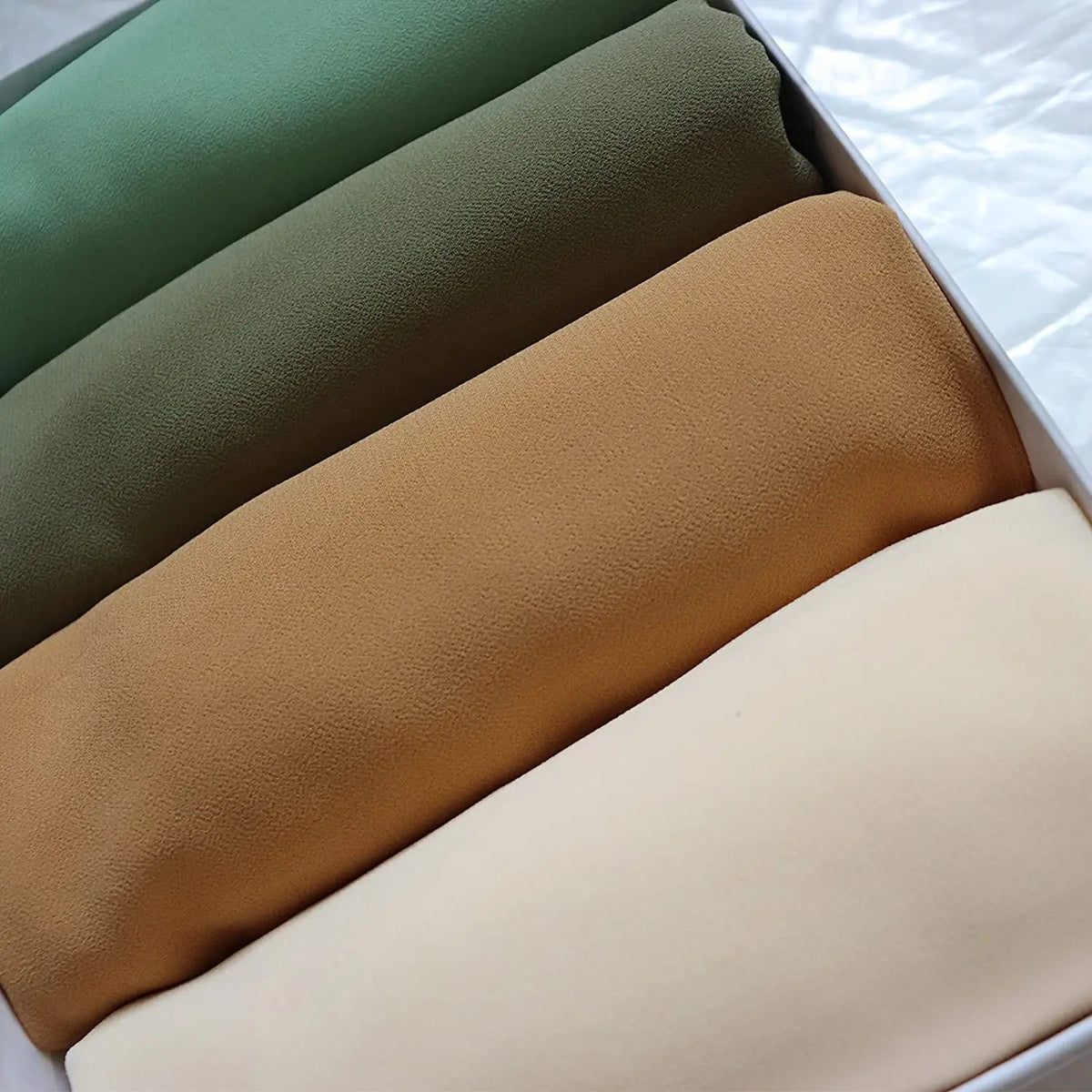 Eine Stapel von vier schlichten Chiffon-Hijabs oder Instant-Schals in Olivgrün, Beige und Tan, von der Seite betrachtet.