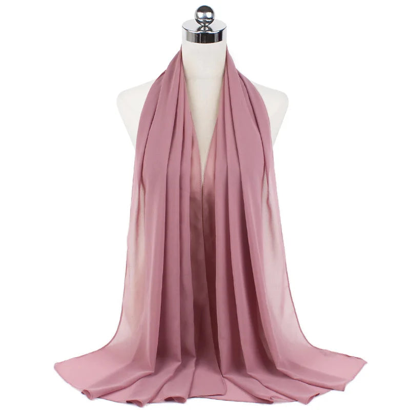 Pañuelo de chifón rosa polvoriento y fluido drapeado alrededor del cuello de un maniquí.