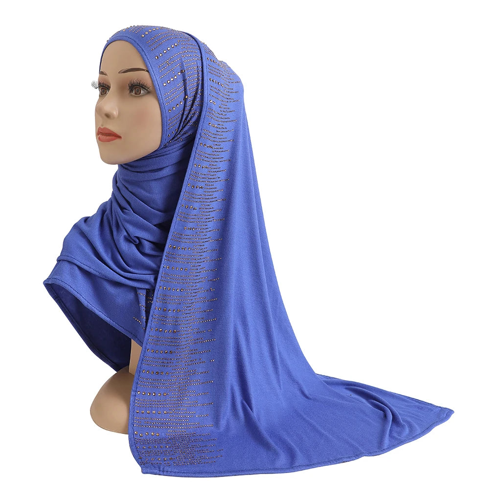 Une femme modèle un foulard en jersey de coton bleu royal avec des accents de diamant drapé sur sa tête et son épaule.
