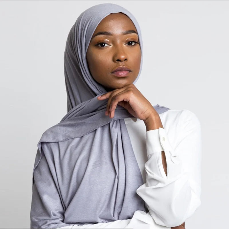 Eine Frau trägt einen grauen Baumwoll-Jersey-Hijab und ein weißes Hemd.