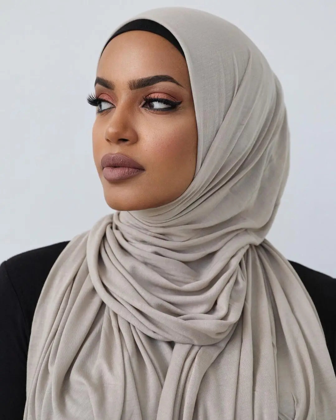 Une femme portant un foulard de jersey en coton beige avec un sous-voile noir et un maquillage foncé.
