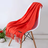 Un chal de cachemira naranja brillante colgado sobre una silla blanca con patas de madera.