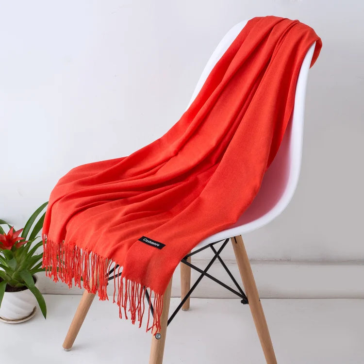 Un chal de cachemira naranja brillante colgado sobre una silla blanca con patas de madera.