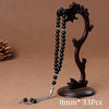A dark brown prayer bead necklace with a tassel is displayed on a wooden stand.