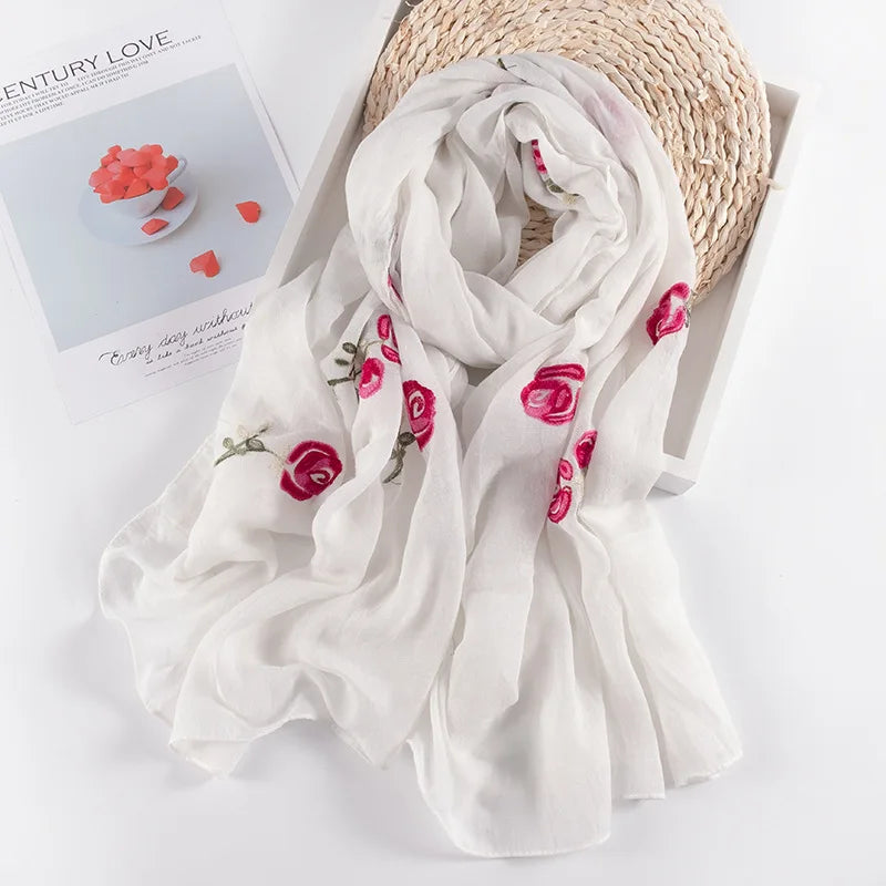 Weißes, florales, besticktes Wintertuch neben einem natürlichen Korb und rosa Blütenblättern.