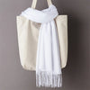 Una bolsa tote beige con un chal de cachemira blanca drapeado sobre la parte superior.
