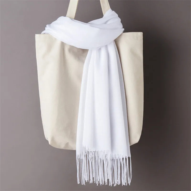 Una bolsa tote beige con un chal de cachemira blanca drapeado sobre la parte superior.