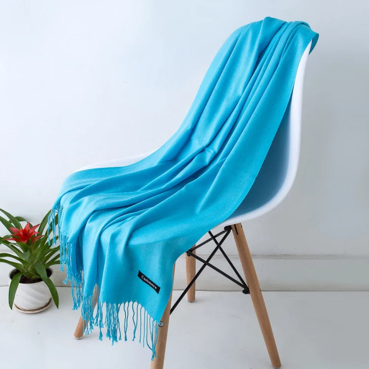 Un chal de cachemira azul brillante drapeado sobre una silla blanca, con detalles de flecos.