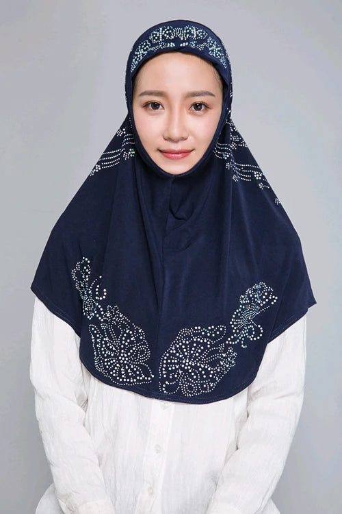 Eine Frau trägt einen dunkelblauen Diamant-Hijabschal über einem weißen Oberteil.