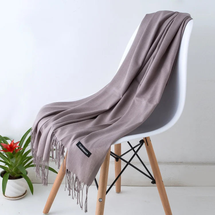 Un chal de cachemira gris colgado sobre una silla moderna con patas de madera y acentos metálicos negros.