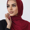 Une femme portant un foulard hijab en jersey de coton couleur marron foncé, regardant sur le côté.