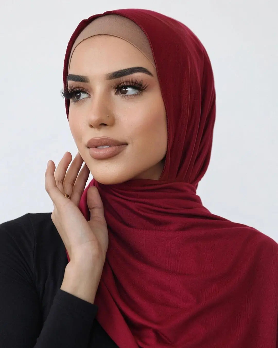 Une femme portant un foulard hijab en jersey de coton couleur marron foncé, regardant sur le côté.
