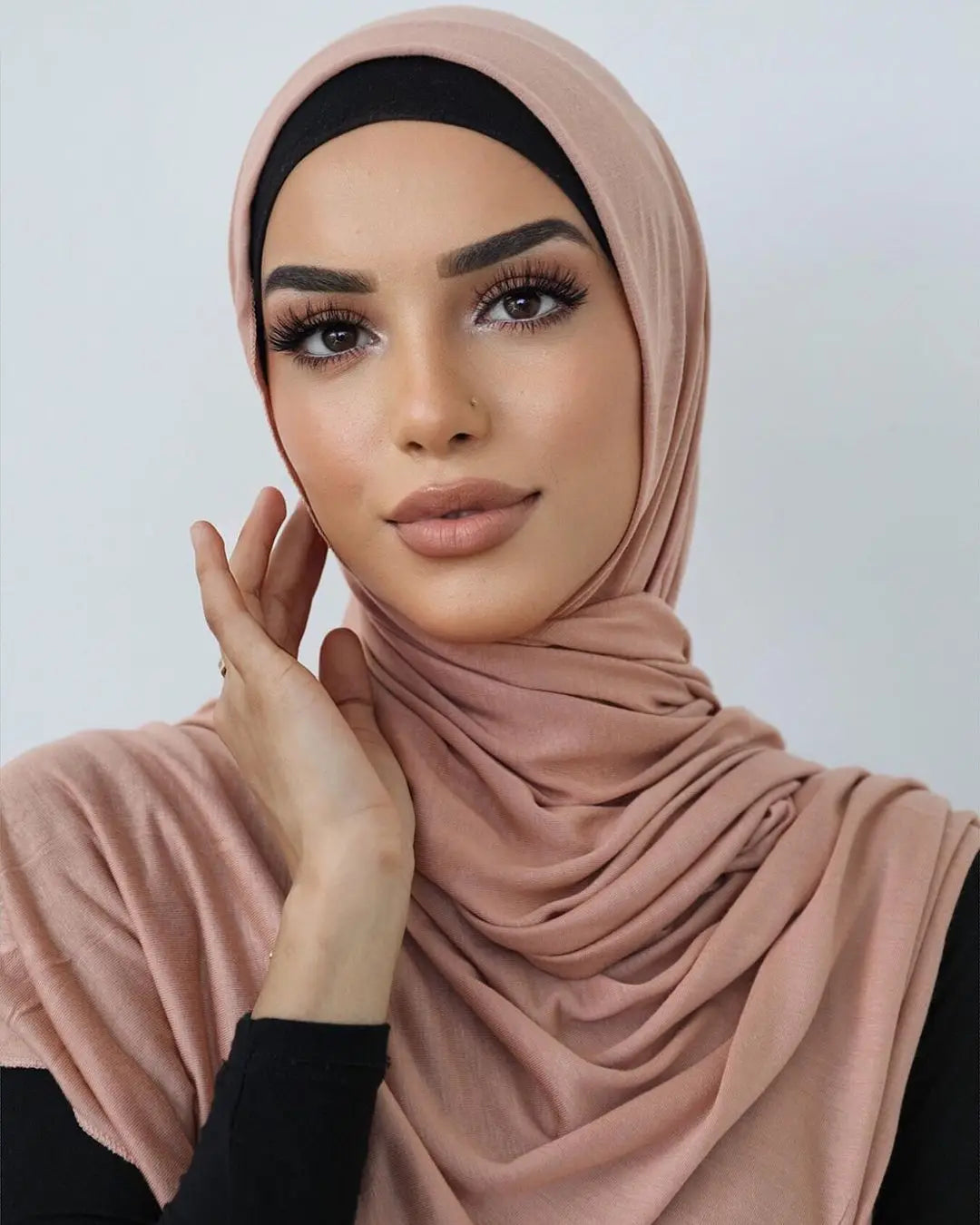 Une femme portant un foulard de jersey en coton couleur rose poudré avec un haut noir.