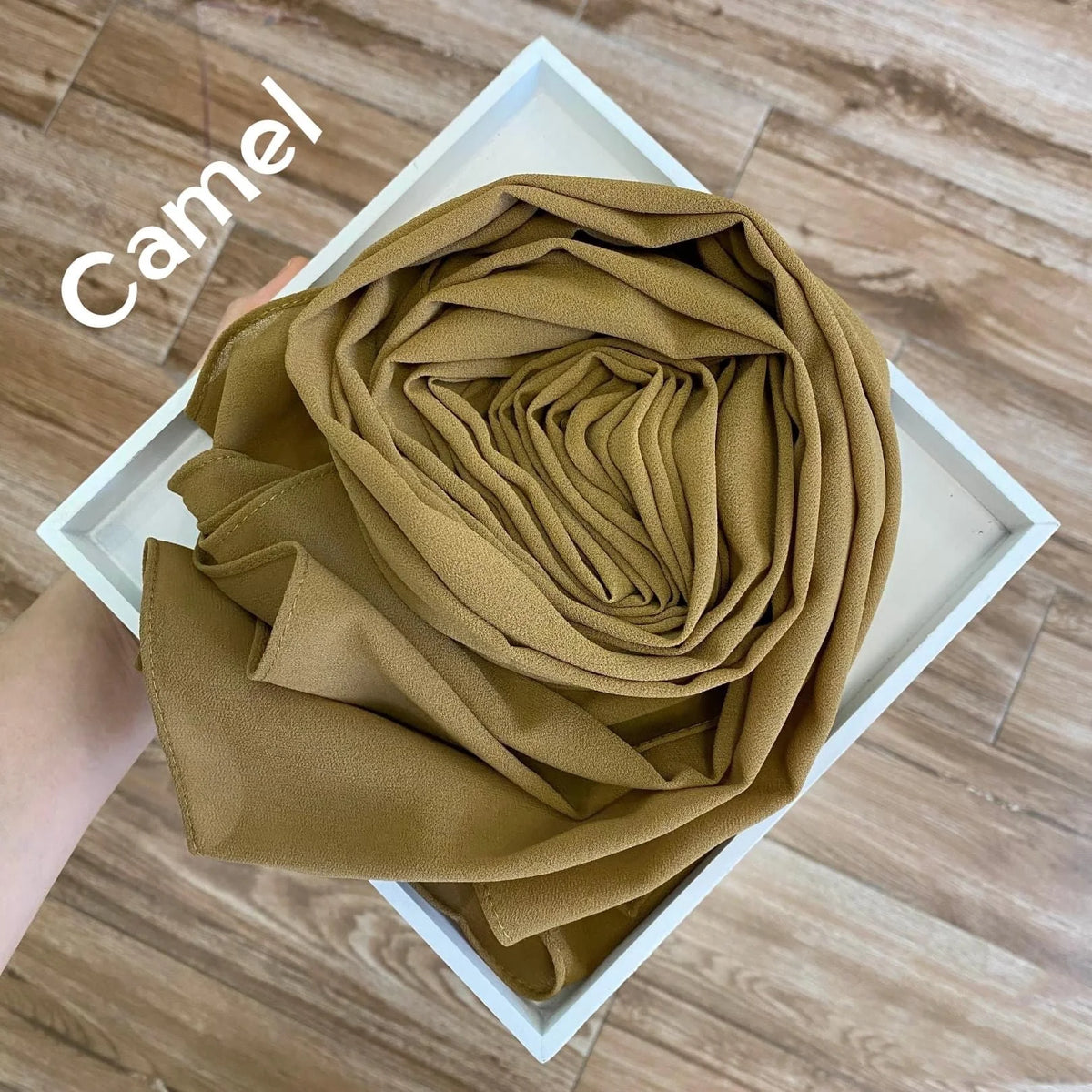 Eng zusammengerollter, fester, kamelfarbener Chiffon-Hijab-Schal in einem weißen Rahmen.