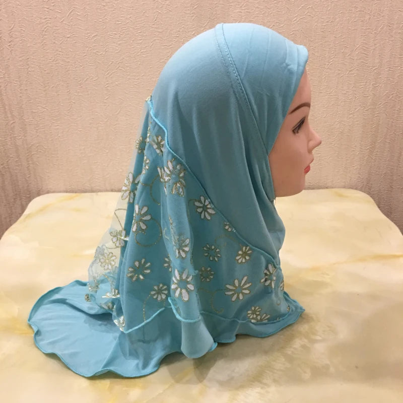 Hellblaue Blumen-Net-Hijab-Kappe, getragen von einer Frau, im Profil vor gelbem Hintergrund.