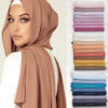 Eine Frau modelliert einen beige Chiffon-Hijabschal mit einem weißen Oberteil, neben einem Stapel farbiger Chiffonschals.