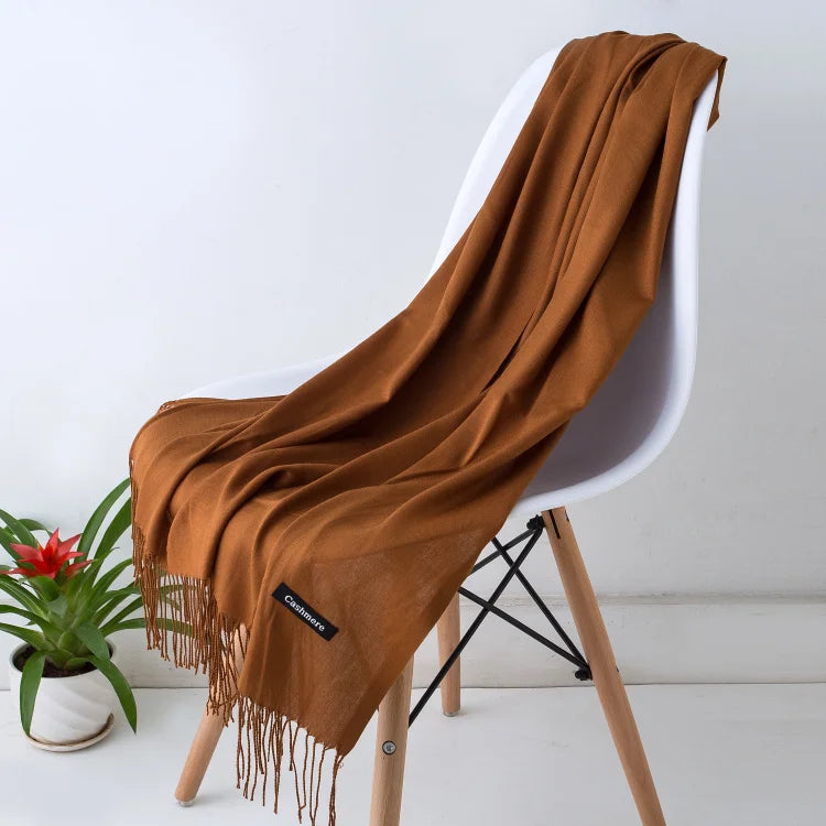 Un chal de cachemira marrón drapeado sobre una silla blanca con patas de madera.