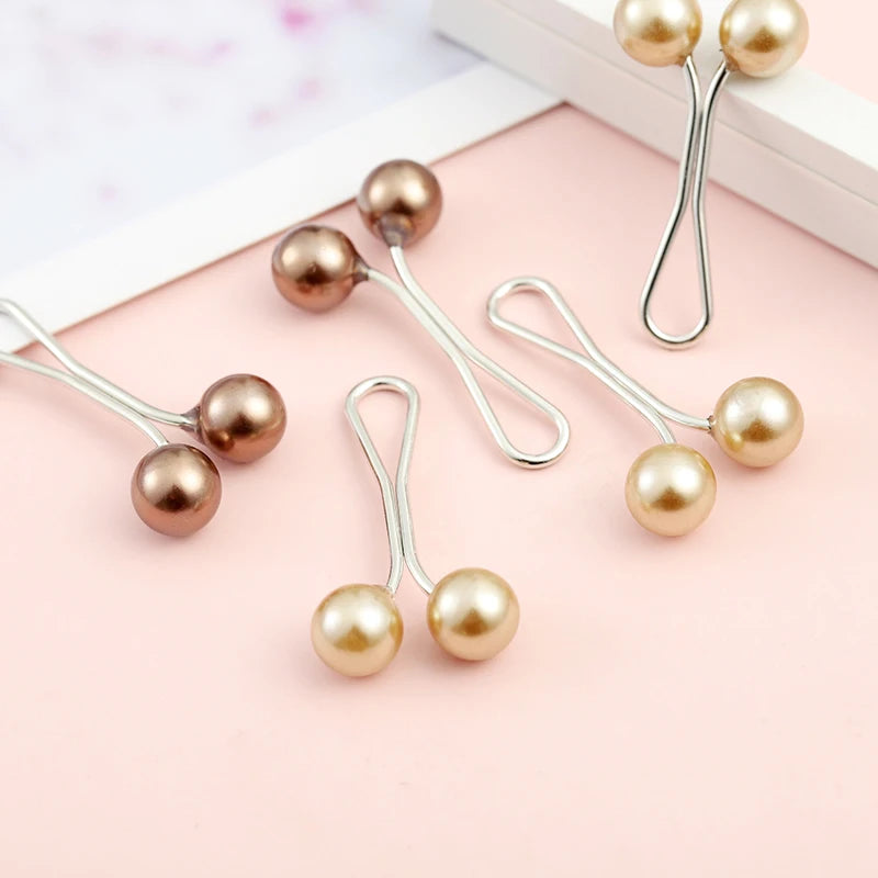A collection of 12 pearl brooch headscarf pins in gold-toned metal and pearl-colored beads arranged on a pink surface.