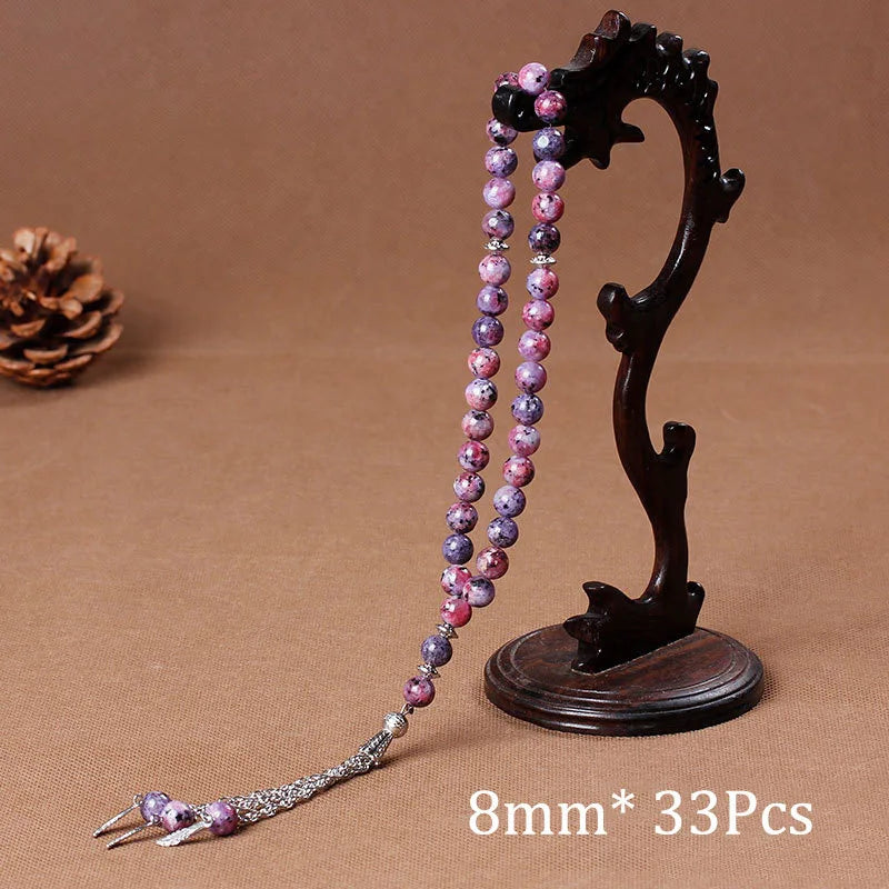 Black agate prayer beads on a dark wooden stand with a long purple beaded tassel necklace