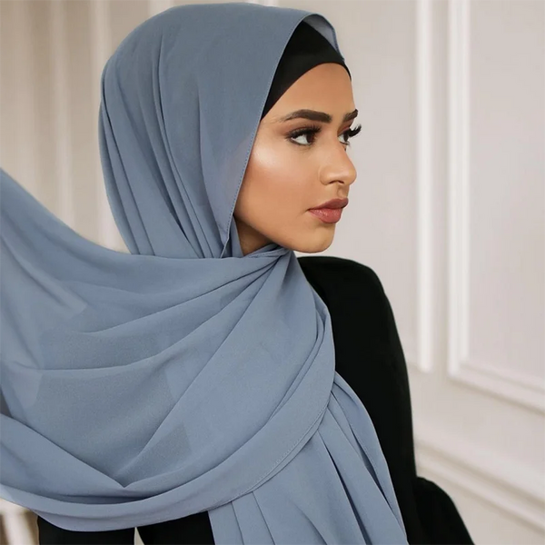 A woman wearing a light blue chiffon hijab draped over her head and shoulders.
