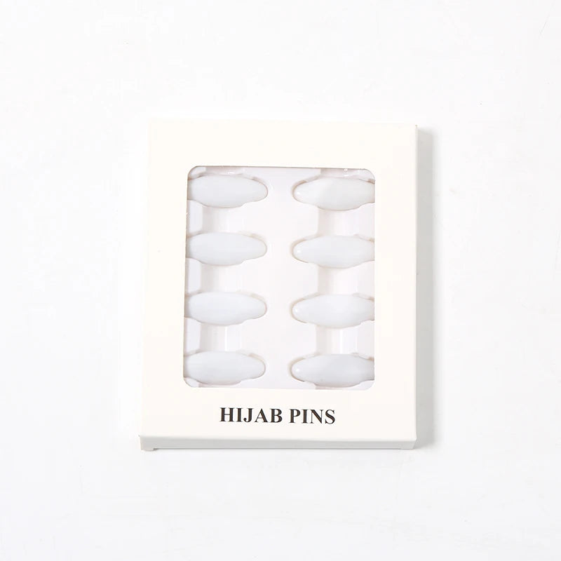 Una caja rectangular blanca que contiene ocho chinchetas y clips translúcidos para hijab.
