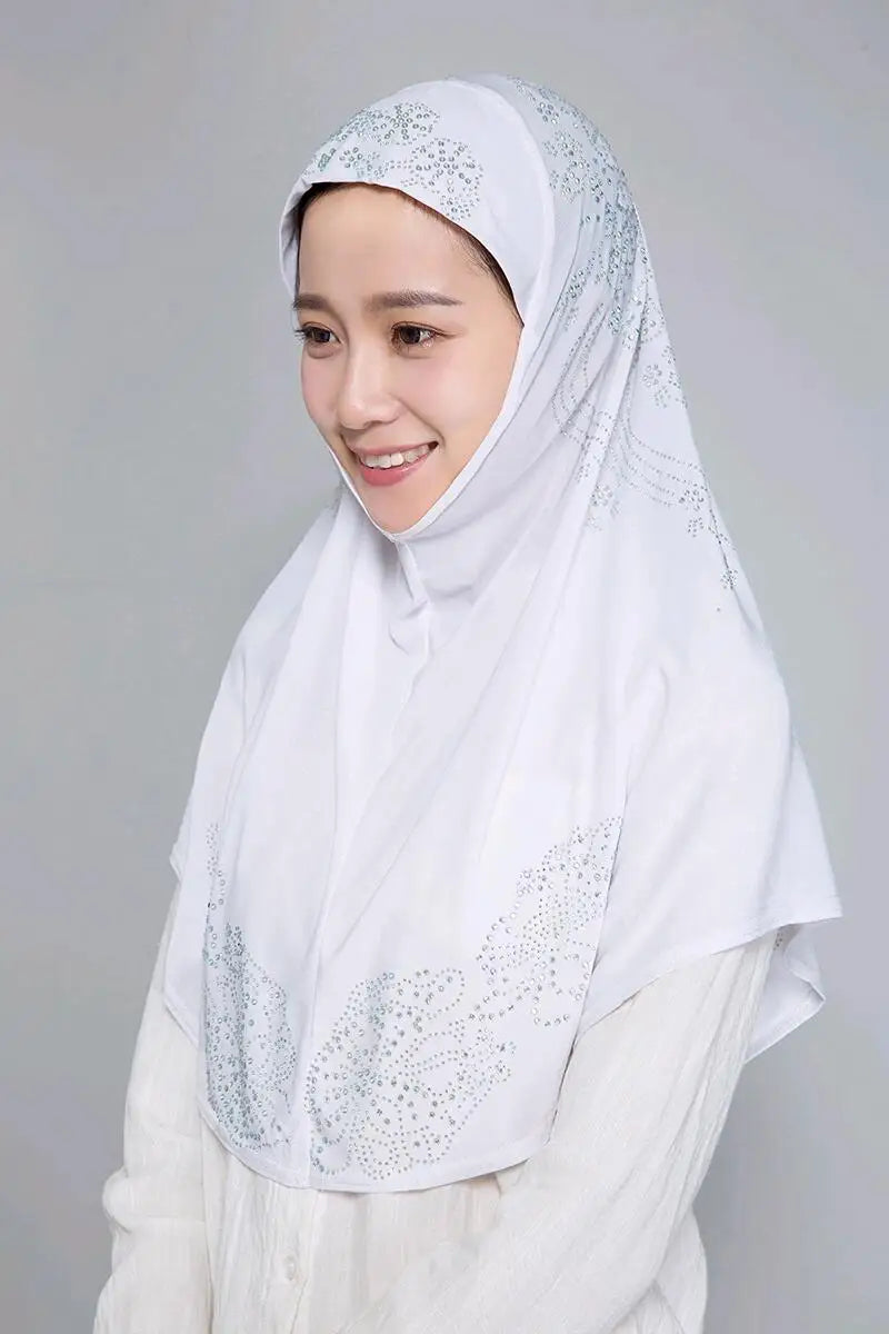 Eine Frau trägt einen eleganten weißen Hijab mit silbernen Strass und einem hellen Oberteil.