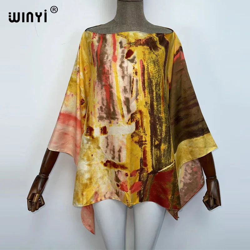 A model is wearing a flowing, multicolored batwing abaya top with abstract vertical stripes in yellow, red, and brown tones.