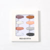 Una caja blanca con ocho chinchetas para hijab en varios tonos beige, rosa y gris.