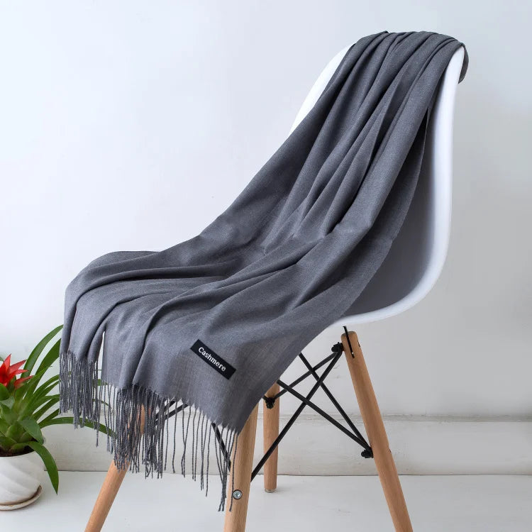 Un chal de cachemira gris drapeado sobre una silla de madera, mostrando su textura y bordes flecos