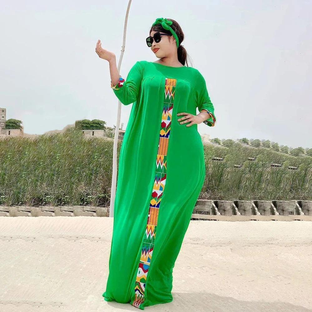 Eine Frau in einem leuchtend grünen Kaftan-Set mit farbenfroher Stickerei steht draußen vor einer trockenen Landschaft.