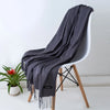 Una chal de cachemira gris oscuro drapeada sobre una silla moderna con patas de madera.