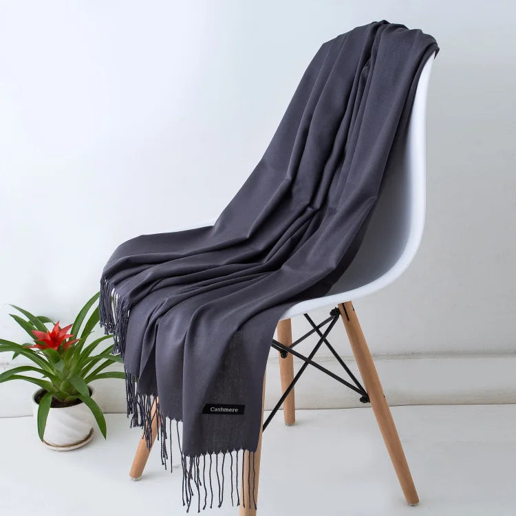 Una chal de cachemira gris oscuro drapeada sobre una silla moderna con patas de madera.