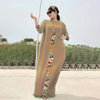 Eine Frau in einem beigen Kaftan-Set mit farbenfroher Stickerei steht draußen vor einer trockenen Landschaft.
