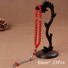 A black wooden prayer bead necklace with red beads and a tassel displayed on a brown fabric.