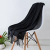 Una chal de cachemira negra drapeada sobre una silla moderna con patas de madera.