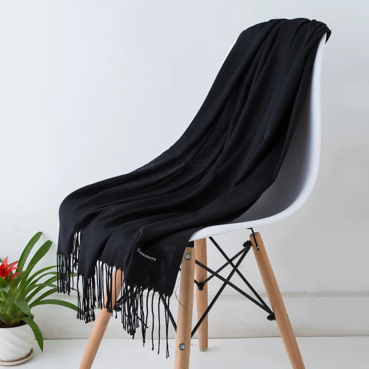 Una chal de cachemira negra drapeada sobre una silla moderna con patas de madera.