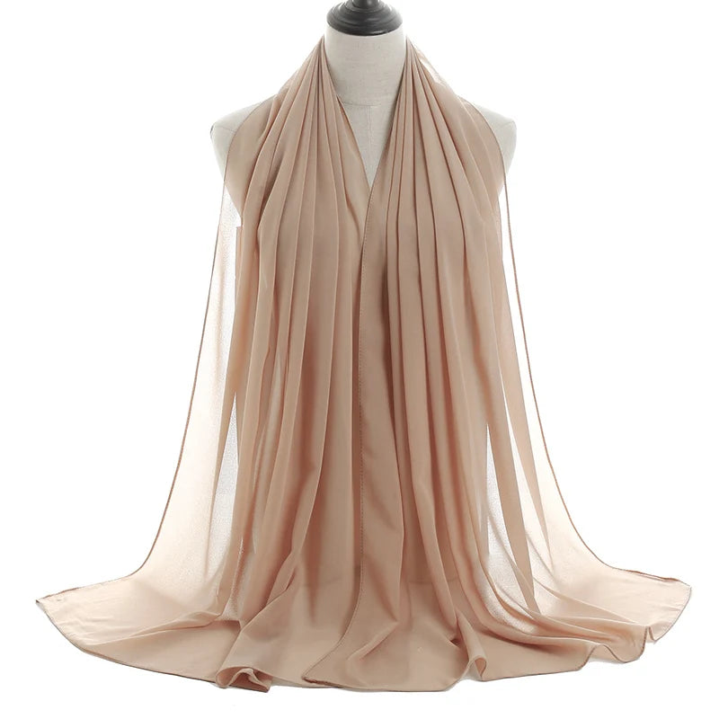 Un pañuelo de chifón beige claro y fluido drapeado alrededor del cuello y los hombros de un maniquí.