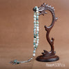 A dark wood prayer bead necklace with light green and white beads and a tassel, displayed on a stand.