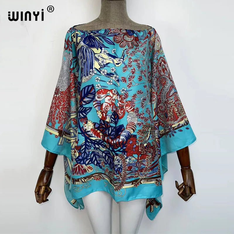 A woman models a colorful bohemian summer batwing abaya top featuring intricate floral and animal patterns in shades of blue,