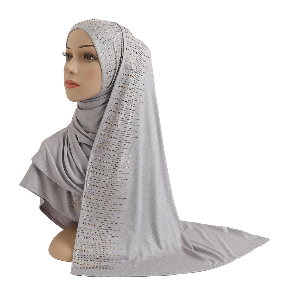 Une femme modèle une écharpe en jersey de coton gris clair et élégante avec des accents diamantés drapée sur sa tête et ses é