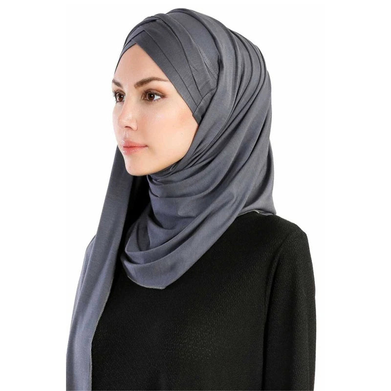 Une femme portant un foulard en jersey de coton gris uni drapé sur sa tête et ses épaules.
