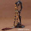 A dark wooden prayer bead necklace with amber beads and a tassel displayed on a stand.