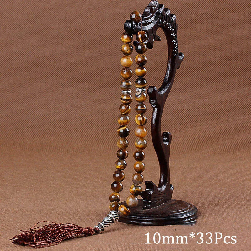 A dark wooden prayer bead necklace with amber beads and a tassel displayed on a stand.