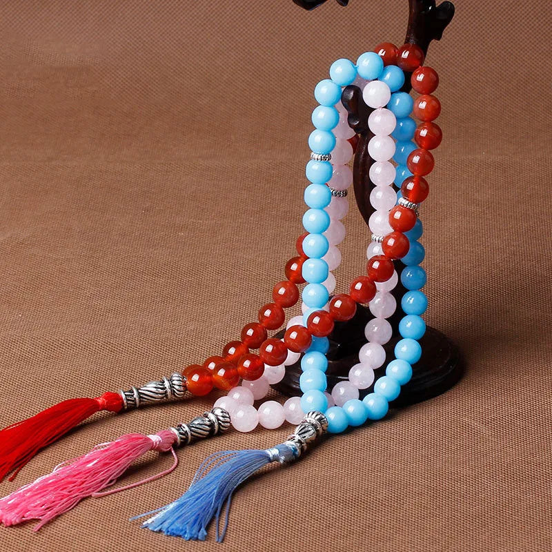 A string of black agate prayer beads in shades of blue and red, featuring colorful tassels.