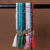 A string of black agate prayer beads with colorful silk tassels hanging on a dark rod.