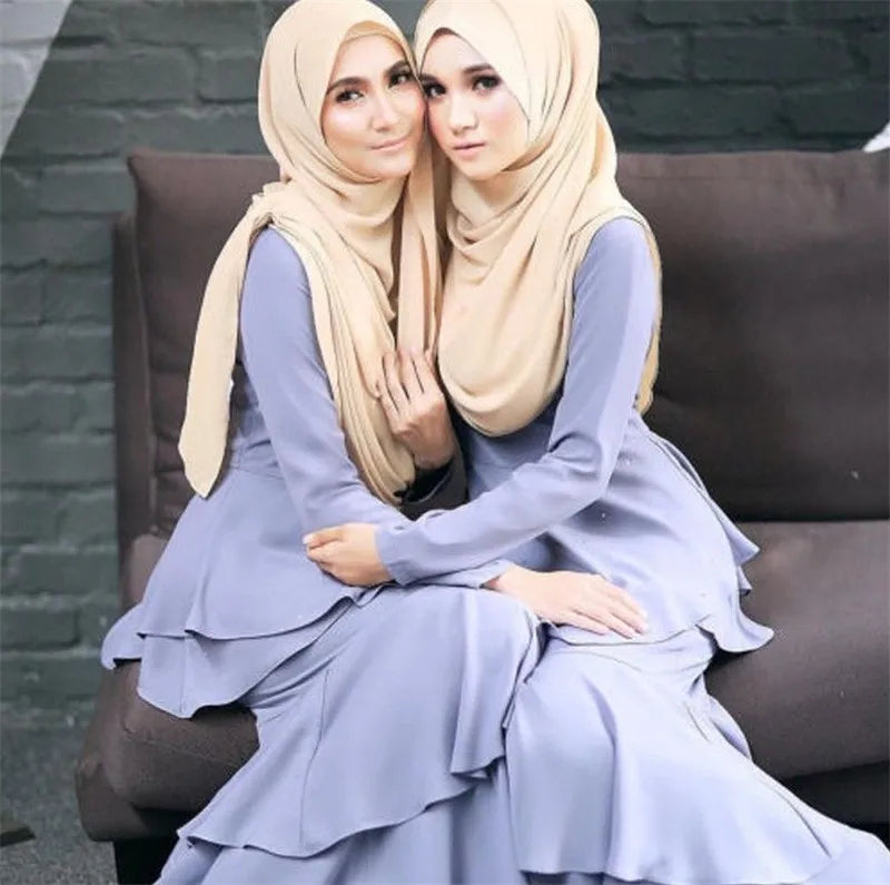 Zwei Frauen tragen elegante, solide Chiffon-Hijabs in Beige- und Lilatönen und sitzen zusammen.