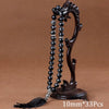 A dark brown wooden prayer bead necklace with black agate beads and a tassel displayed on a stand.